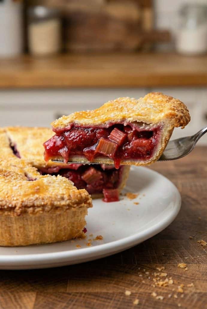 A slice of strawberry rhubarb pie being lifted from the pan, revealing the juicy fruit filling and flaky crust.