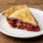 Slice of homemade strawberry rhubarb pie on a white plate, showing the golden crust and vibrant sweet-tart filling featured in the recipe.