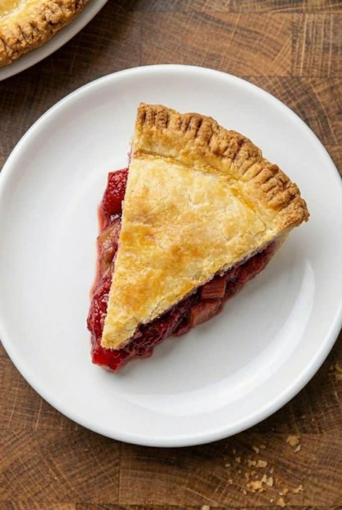 Top view of a slice of strawberry rhubarb pie on a white plate, showcasing the golden crust and vibrant filling.
