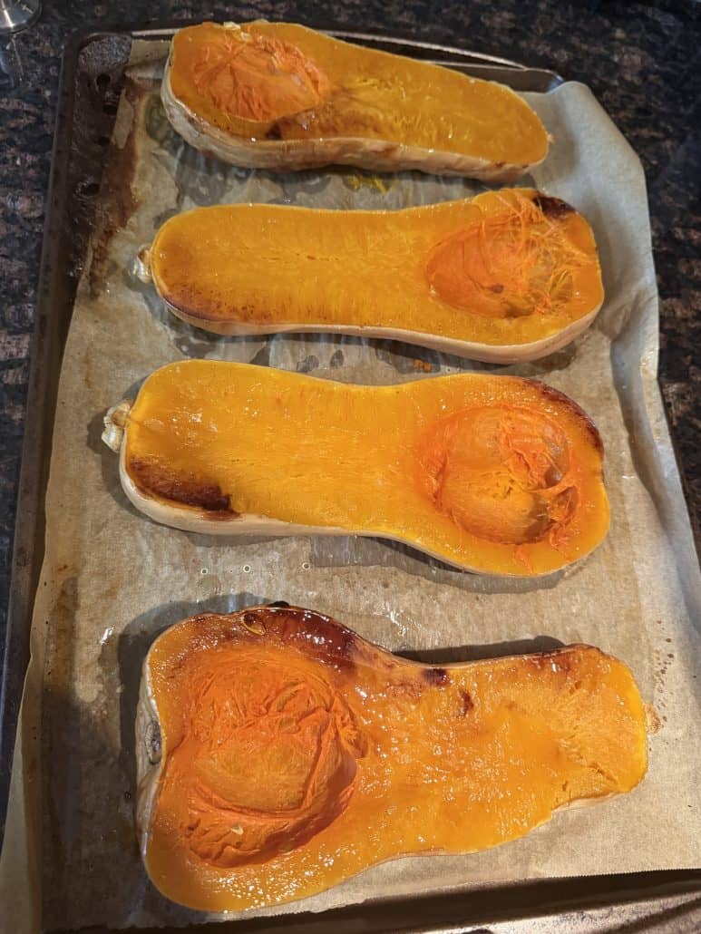 Roasted butternut squash halves placed cut side up on a parchment-lined baking sheet, ready to be stuffed for a vegan main dish.