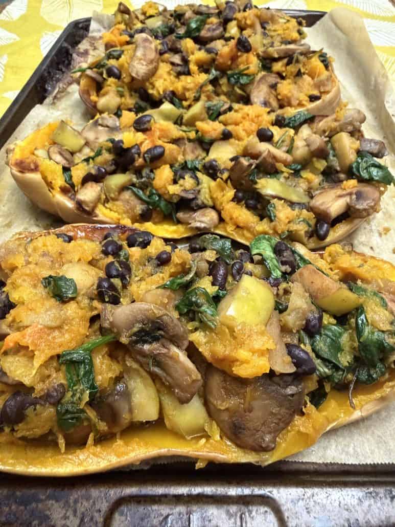 Close-up of baked vegan stuffed butternut squash filled with a colorful mix of mushrooms, black beans, spinach, apples, and roasted squash.
