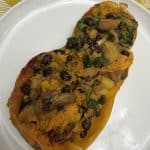 Single serving of vegan stuffed butternut squash with mushrooms, black beans, apples, and spinach, served on a white plate.