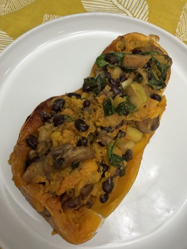 Single serving of vegan stuffed butternut squash with mushrooms, black beans, apples, and spinach, served on a white plate.