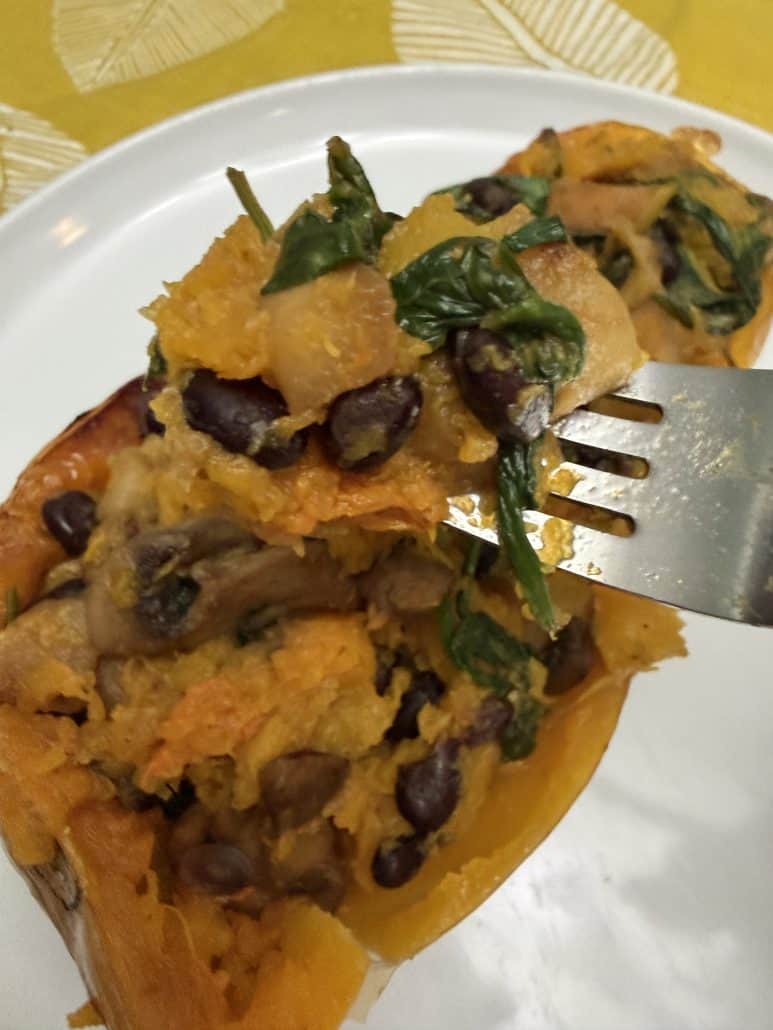 Forkful of vegan stuffed butternut squash showing black beans, spinach, apples, mushrooms, and mashed squash on a white plate.