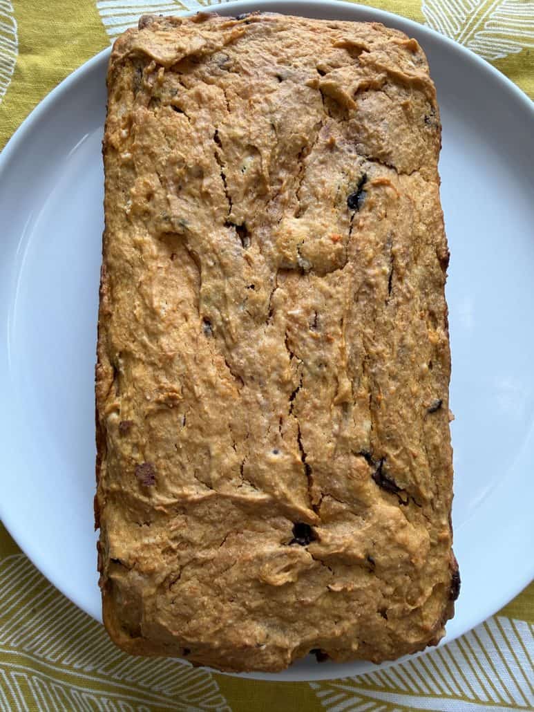 Whole loaf of homemade sweet potato bread on a white plate, ready to slice and serve.
