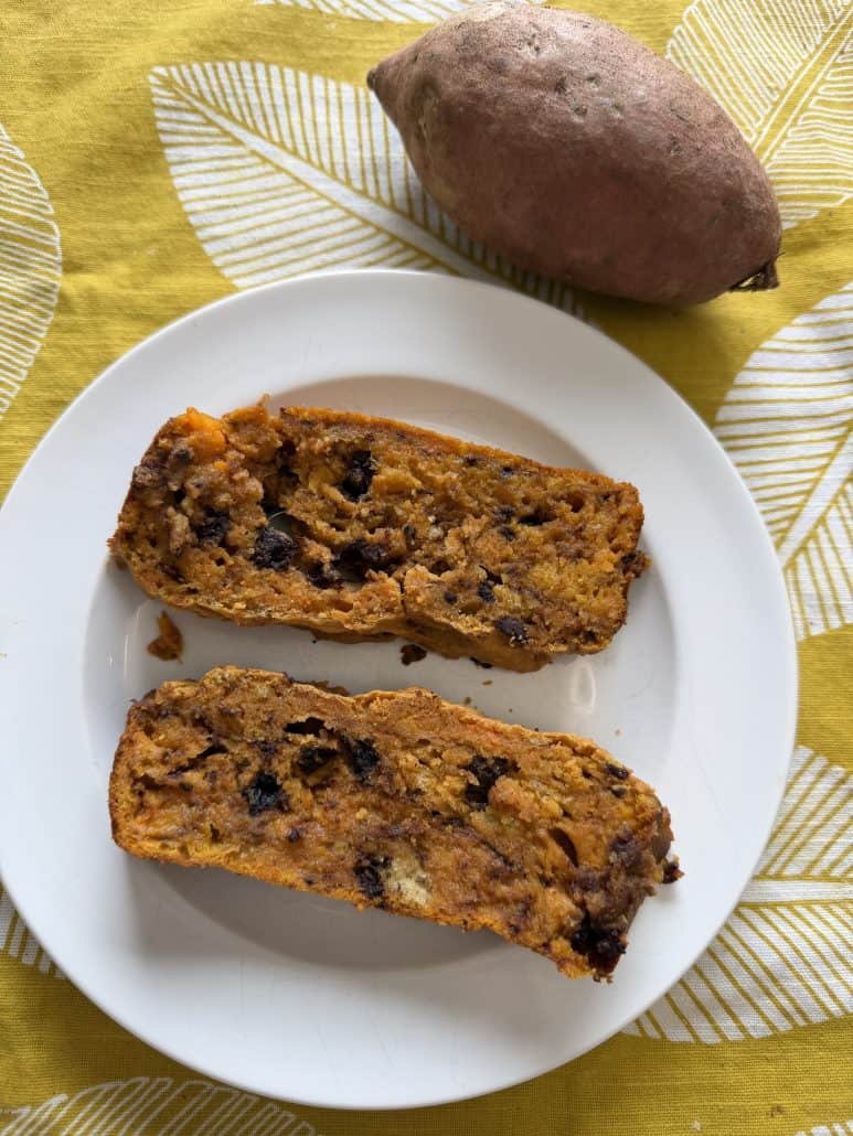 Two slices of sweet potato chocolate chip bread on a plate, with a raw sweet potato nearby.