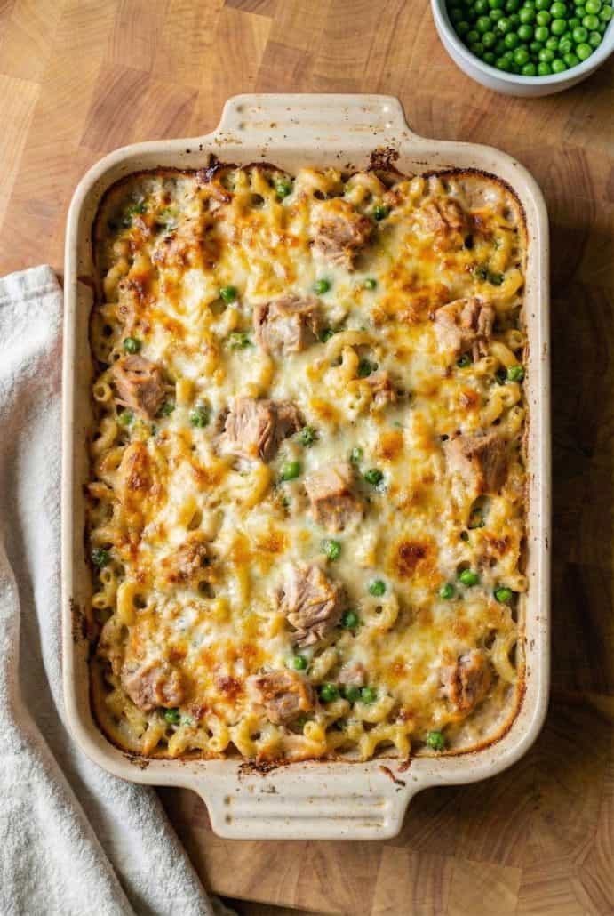 Baking dish filled with golden brown tuna casserole topped with melted cheese and green peas.