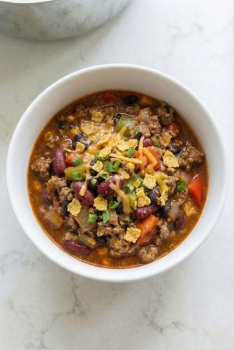How to Make Boilermaker Tailgate Chili | Game Day Recipe Bowl of Boilermaker Tailgate Chili garnished with shredded cheese, chopped green onions, and crushed corn chips.