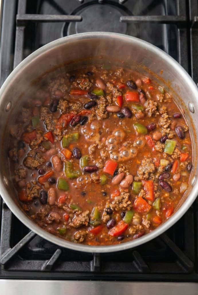 Boilermaker Tailgate Chili bubbling on the stovetop in a large pot, filled with ground beef, beans, and colorful bell peppers for a thick, flavorful chili.