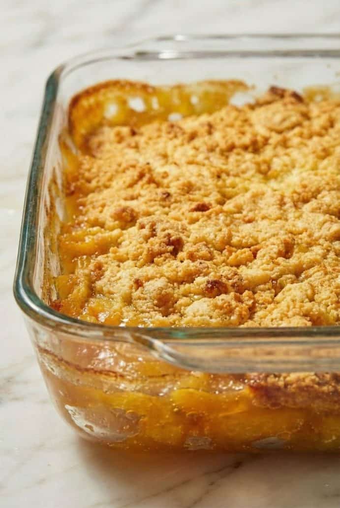 Close-up of golden brown 3 Ingredient Cake Mix Peach Cobbler in a glass dish, showing the bubbly peach filling and crumbly cake mix topping.