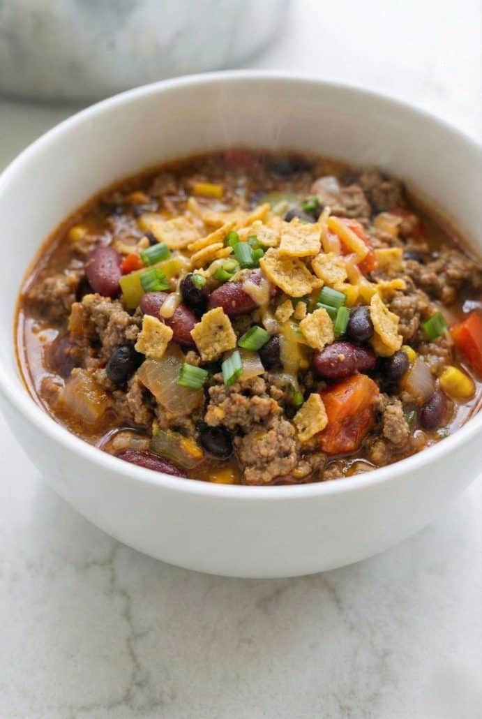 Close-up of Boilermaker Tailgate Chili in a white bowl, topped with crushed corn chips, shredded cheese, and green onions for a hearty and colorful presentation.
