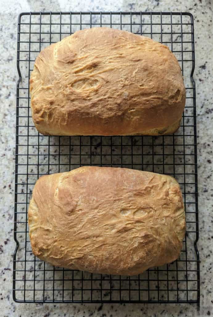 Two loaves of Amish white bread cooling on a wire rack, freshly baked and golden brown.
