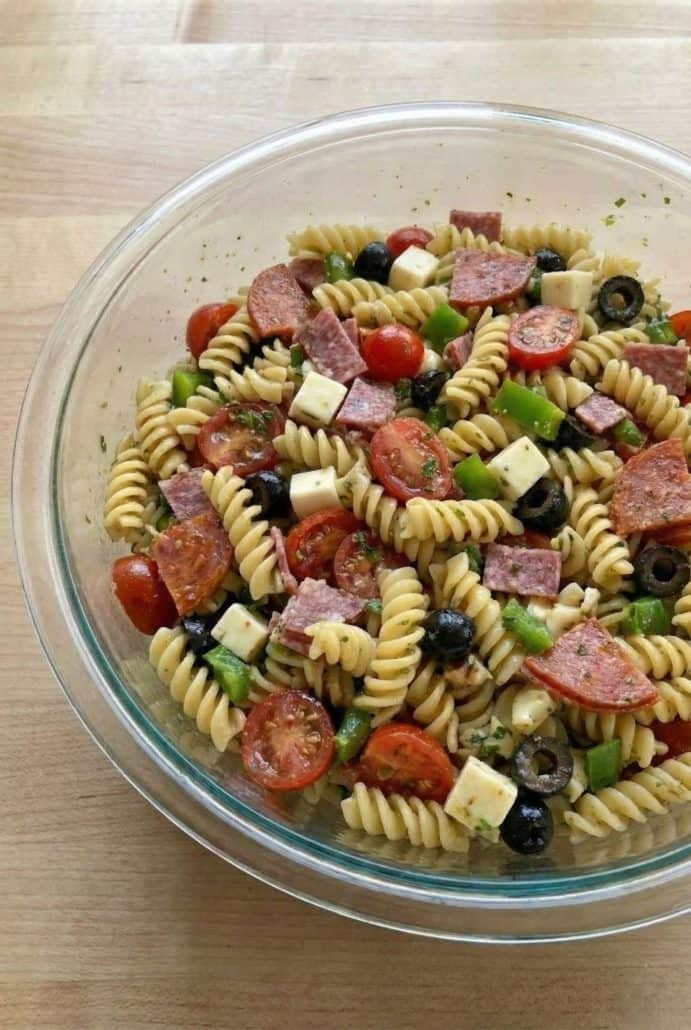 Close-up of Antipasto Pasta Salad in a glass bowl featuring rotini pasta, cherry tomatoes, olives, salami, pepperoni, and cheese.