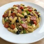 Plate of Antipasto Pasta Salad with rotini, pepperoni, salami, cheese cubes, olives, tomatoes, and bell peppers. Perfect for a make-ahead cold pasta dish.