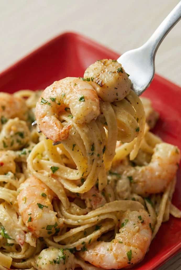 Forkful of creamy Cajun pasta with shrimp and scallops lifted from a red plate.