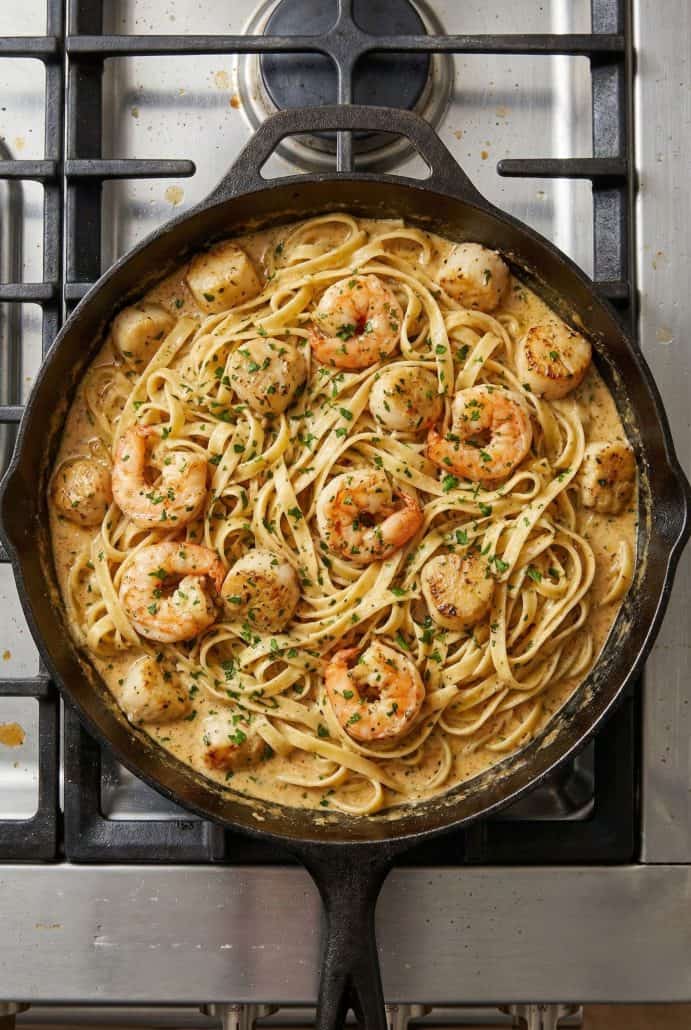 Creamy Cajun seafood pasta with shrimp and scallops simmering in a skillet on the stovetop.