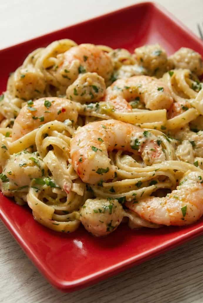 Close-up of creamy Cajun seafood pasta with shrimp and scallops served on a red plate.