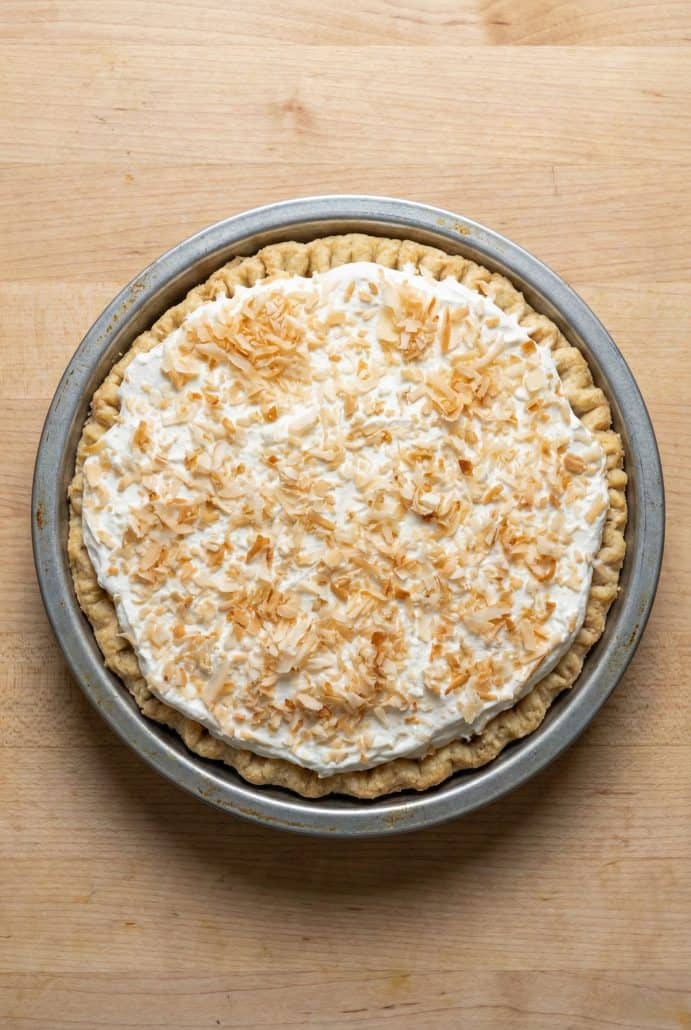 Whole coconut cream pie in a metal pie pan, topped with whipped cream and toasted coconut.