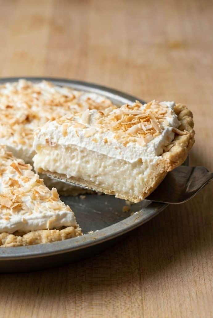 Slice of coconut cream pie being lifted from the pan, showing the creamy filling, flaky crust, and toasted coconut topping.