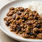 Cuban-style picadillo with ground beef, olives, and raisins served with white rice on a plate. A savory and sweet Latin-inspired dish.