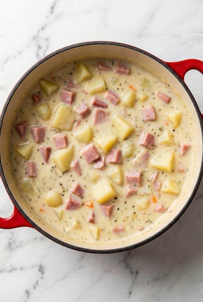 Large pot of creamy ham and potato soup simmering on the stovetop, showing the hearty texture and ingredients.