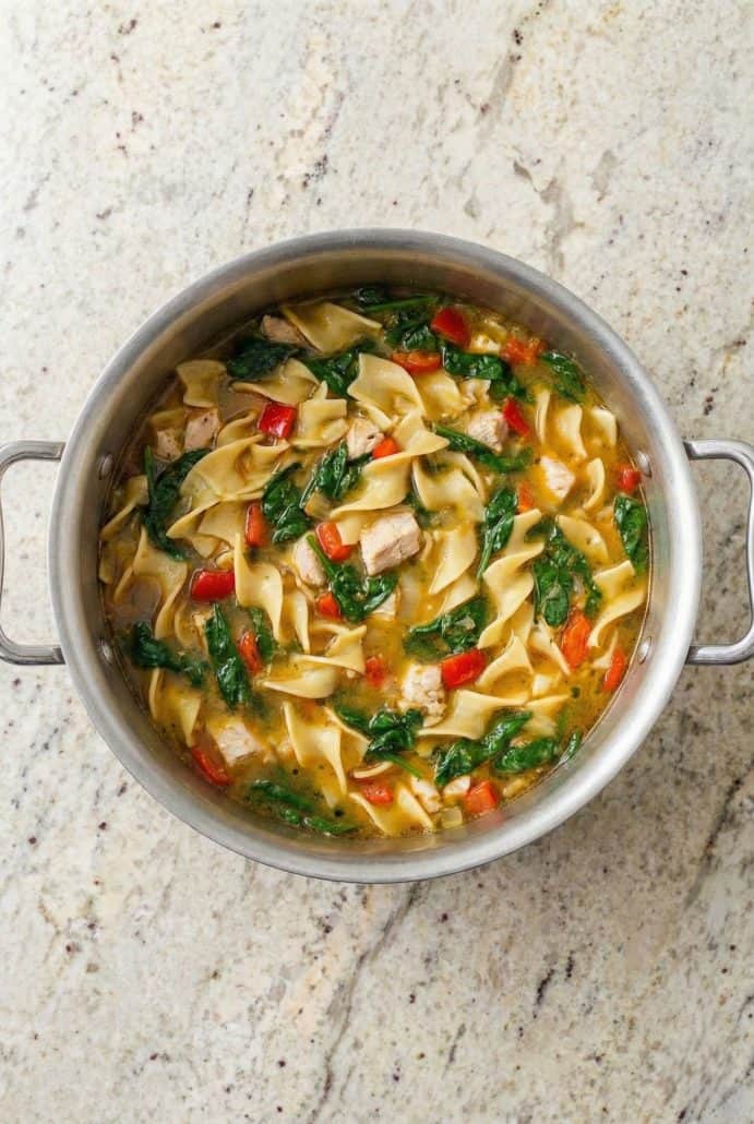 Large soup pot filled with Healthy Chicken Zuppa made with spinach, red bell peppers, egg noodles, and chicken, freshly cooked.