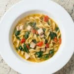 Bowl of Healthy Chicken Zuppa with spinach, red peppers, and egg noodles in a light broth, served as a hearty one-pot dinner soup.