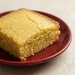 A close-up of a slice of moist, golden healthy cornbread on a red plate, ready to serve.