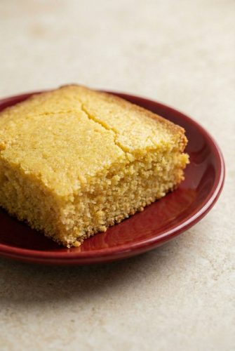 A close-up of a slice of moist, golden healthy cornbread on a red plate, ready to serve.