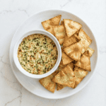 Hearts of palm dip served in a small white bowl with crispy pita chips on the side, perfect for a party appetizer.