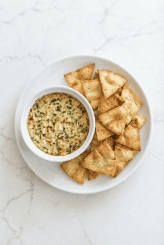 Hearts of palm dip served in a small white bowl with crispy pita chips on the side, perfect for a party appetizer.