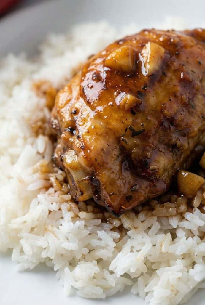 Close-up of a honey-garlic chicken thigh served over fluffy white rice, showcasing the sticky glaze and tender texture from the slow cooker recipe.