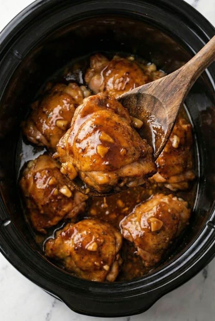 Honey-garlic chicken thighs in a slow cooker with a wooden spoon, showing the saucy, tender result of this easy dump-and-go slow cooker recipe.