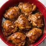 Tender honey-garlic chicken thighs in a red bowl, coated in a sticky, slow-cooked sauce.