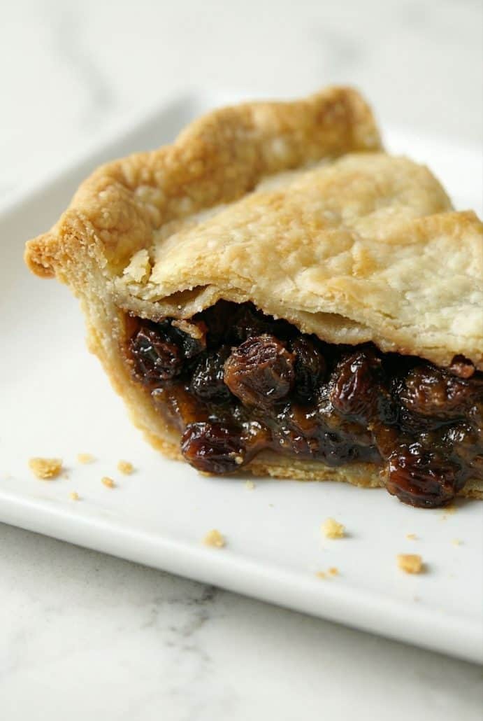 Close-up of a slice of old fashioned raisin pie on a white plate, highlighting the gooey raisin filling and crisp, golden crust.