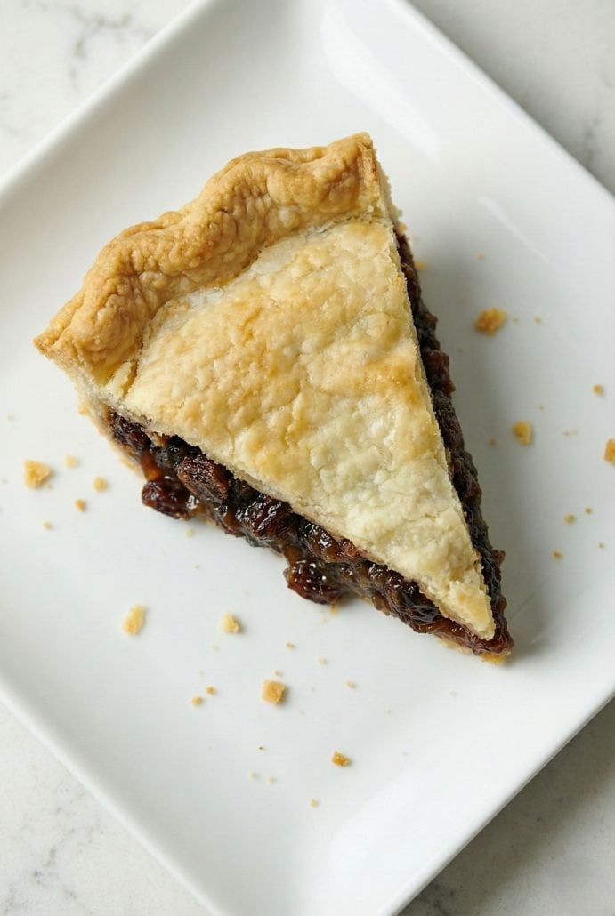 Top view of a single slice of old fashioned raisin pie on a white plate, showcasing the flaky crust and rich filling.