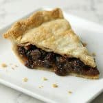 Slice of old fashioned raisin pie on a white plate, showing the thick raisin filling and golden flaky crust.