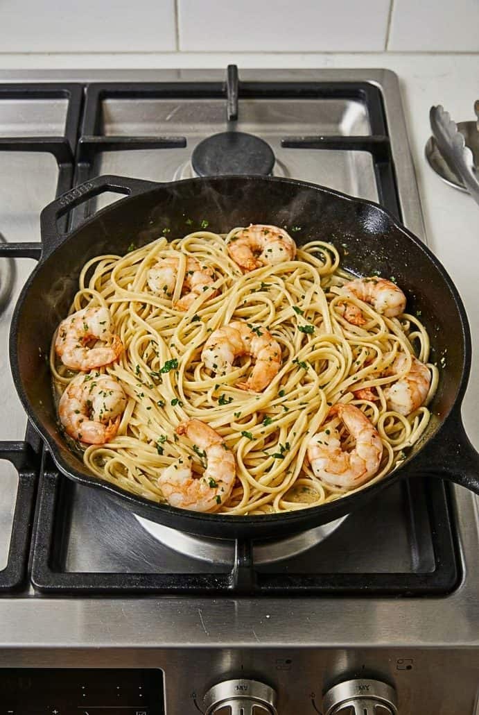 Garlic butter shrimp scampi with linguine cooking in a skillet on the stovetop.