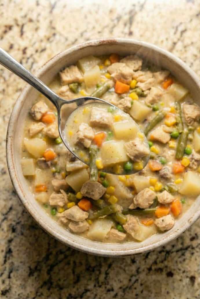 Spoonful of hearty Chicken Pot Pie Stew being lifted from a bowl, showing chunks of chicken, potatoes, carrots, and mixed vegetables in a creamy sauce.