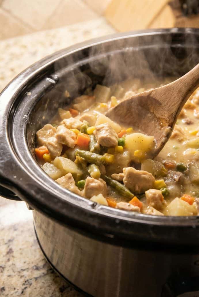 Steamy Slow Cooker Chicken Pot Pie Stew being stirred with a wooden spoon, showing tender chunks of chicken, potatoes, and vegetables in a creamy broth.