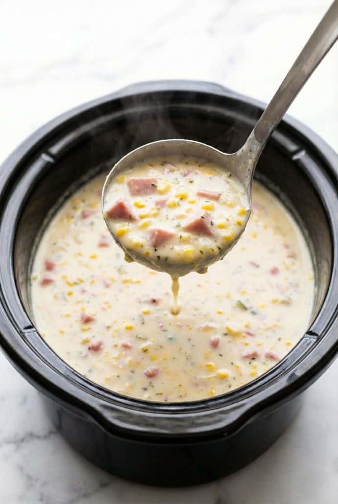 Ladle of hot slow cooker corn chowder with ham, potatoes, and corn being served from the crockpot.