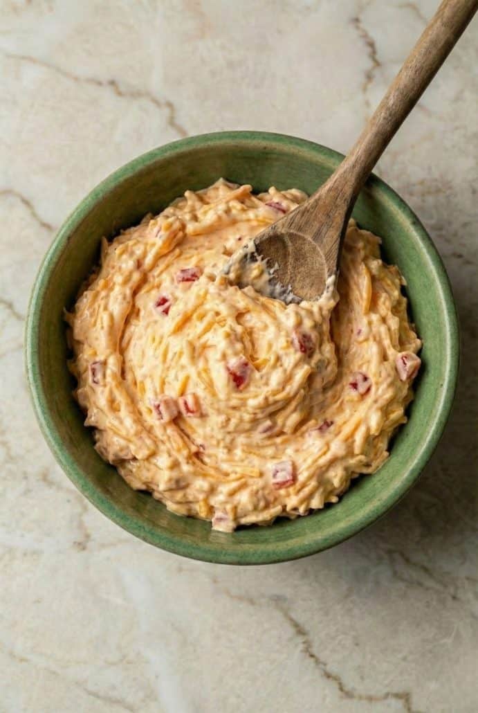Homemade pimento cheese in a green bowl with a wooden spoon. A creamy, flavorful Southern spread ready to serve.