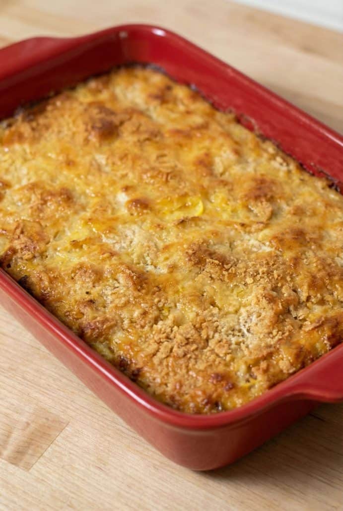 Close-up of golden baked squash casserole in a red dish, showcasing the crispy cracker and cheese topping.