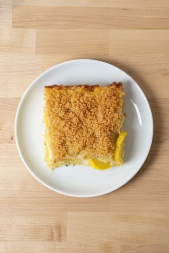 Single serving of baked squash casserole on a white plate, showing the crispy cracker topping and tender squash layers.