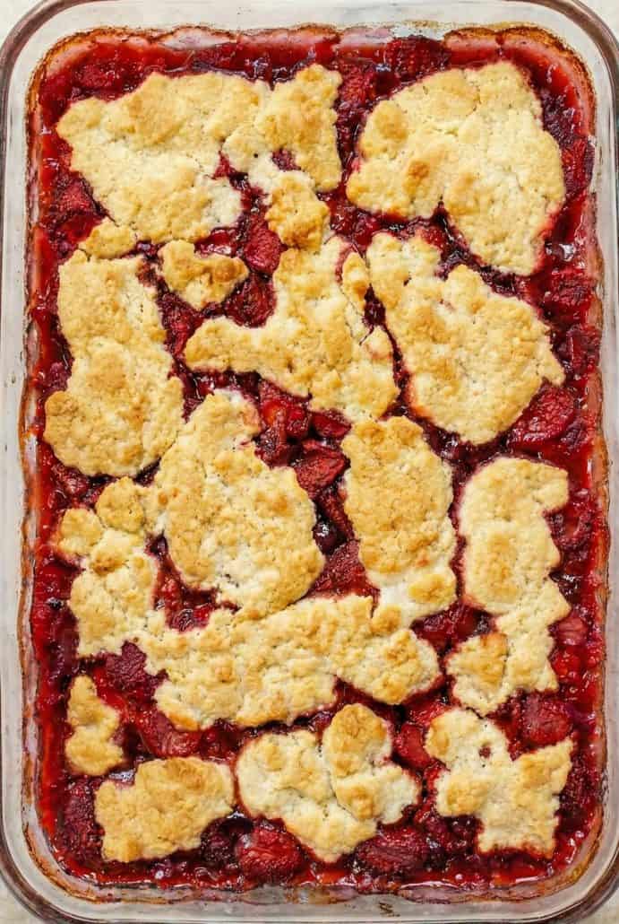 Freshly baked strawberry cobbler with golden biscuit topping in a glass baking dish.