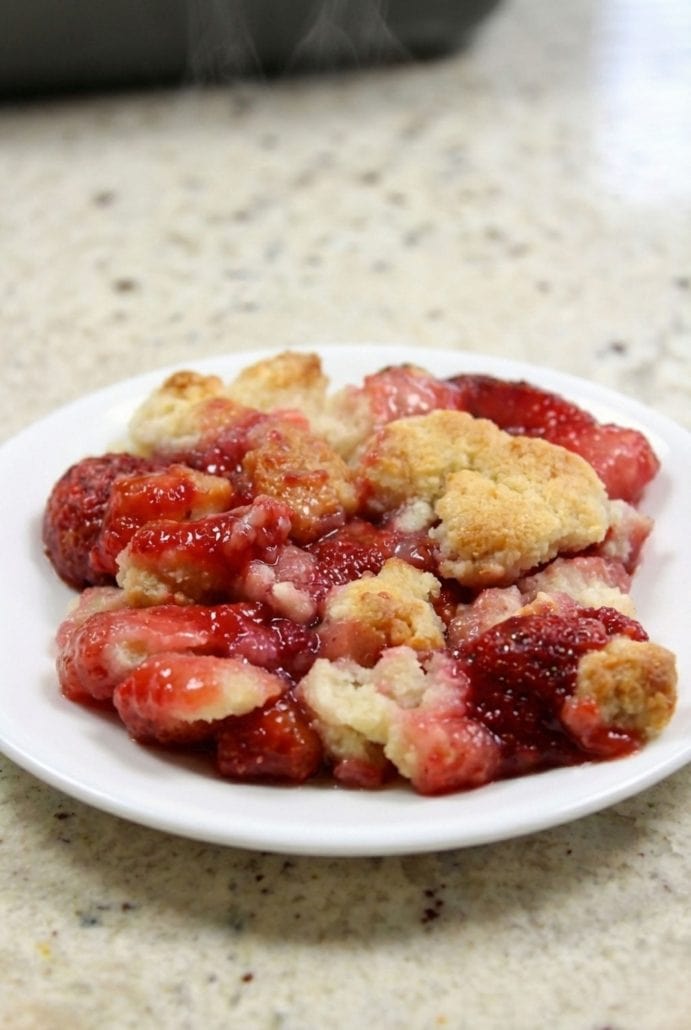 Warm strawberry cobbler served on a white plate, showing juicy filling and golden topping.
