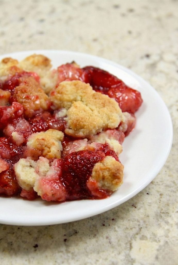 Close-up of strawberry cobbler on a white plate showing juicy berries and golden baked topping.
