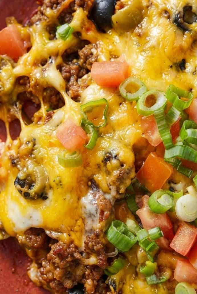 Close-up of cheesy taco casserole with ground beef, black olives, tomatoes, and green onions. Detailed look at the layers in the Taco Casserole recipe.