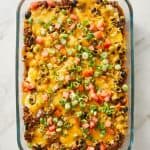 Cheesy taco casserole topped with chopped tomatoes and green onions in a glass baking dish.