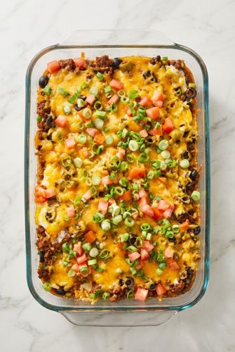 Cheesy taco casserole topped with chopped tomatoes and green onions in a glass baking dish.